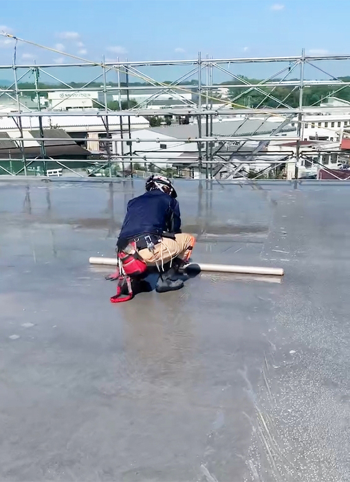 一人の社員がロール状の資材を扱う作業をしている、ビルの屋上